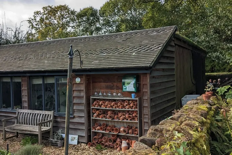 A timber-clad garden building with a tiled roof behind a dry-stone wall